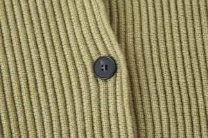 Macro detail of olive green ribbed knit fabric and black four-hole button on cardigan