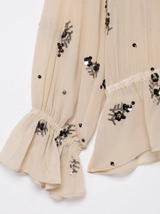 Detailed view of beige translucent blouse with black sequin embroidery and ruffled cuffs