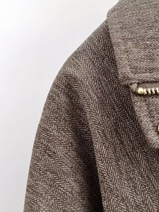 Details von braunem Fischgrätmuster und goldenem Reißverschluss an der Jackenschulter