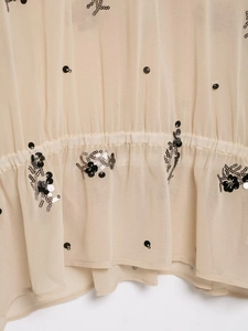 Detail of sheer beige blouse featuring sequined floral patterns and elastic pleats