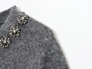 Detail of grey knit sweater showing luxury jewel flower embellishments on the neckline