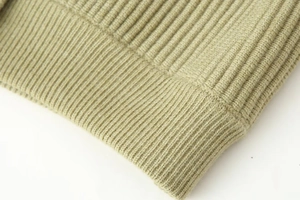 Macro shot of fine ribbed knitting details on the light sage green cardigan sleeve