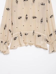 Detail of sheer beige blouse with black sequin floral embroidery and ruffled cuffs