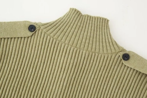 Detail of sage green knit sweater with high collar and decorative black buttons on shoulders