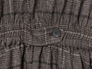 Detailed macro view of the elastic waist with dark button and textured plaid fabric