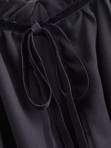 Detail of elegant black blouse featuring velvet trim and a delicate satin bow tie detail