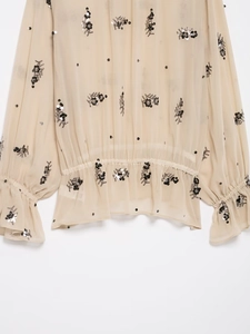 Detail of sheer beige chiffon shirt with black sequin floral embroidery and smocked waist
