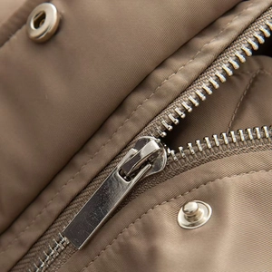 Detail of khaki jacket showing high-density fabric texture with metal zipper and snap button