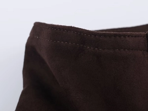 Detailed macro shot of dark brown suede jacket showing reinforced stitching and raw edges
