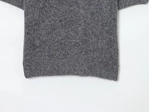 Detailed macro view of the soft grey knit fabric texture and hem on a beaded sweater