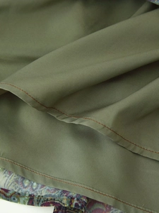 Detail of olive green dress fabric with contrast stitching and paisley lining accents