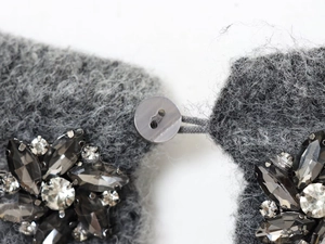 Detail of grey fluffy knitwear showing jewel bead floral accents and a button closure