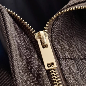 Detailaufnahme des goldenen Reißverschlusses an einer braunen Fischgräten-Jacke aus Stoff