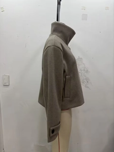 Détail d'un manteau court taupe en laine avec col montant et boucles sur les poignets