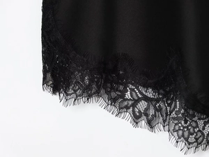 Detailed close-up of smooth black satin fabric with intricate eyelash lace trim edges