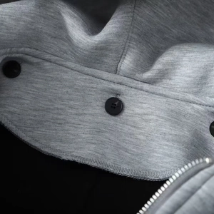 Detailed close-up of grey hooded coat fabric with black buttons and metal zipper detail