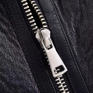 Détail de la fermeture éclair en métal argenté sur un gilet en similicuir noir texturé
