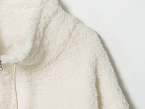 Close-up of a white sherpa fleece jacket featuring a high collar and metal zipper detail