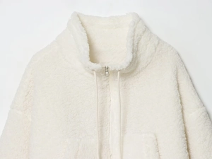 Detail of white sherpa fleece jacket featuring high collar and metallic silver zipper