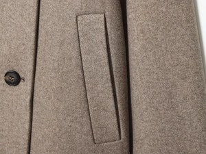 Détail du tissu en laine camel avec bouton marron et coutures de poche verticales