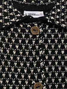 Detail of knit cardigan collar featuring geometric pattern, brand label, and marble buttons