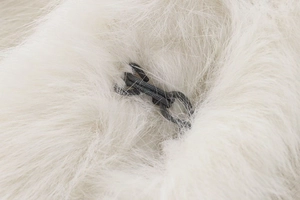 Detailed macro view of the dark grey woven rope buckle on a white faux fur vest fabric