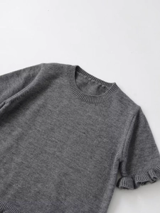 Dettaglio della manica a balze su un maglione grigio a maniche corte in maglia fine