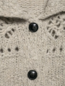 Close-up of thick beige hollow-out knit cardigan showing marbled black buttons and texture