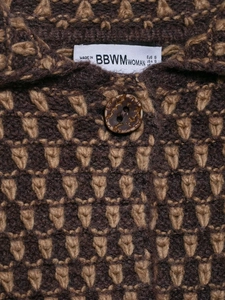 Close-up of textured geometric knit cardigan with marble button and brand neck label