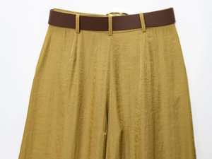 Detail of golden pleated wide leg pants with metallic sheen and brown matte leather belt