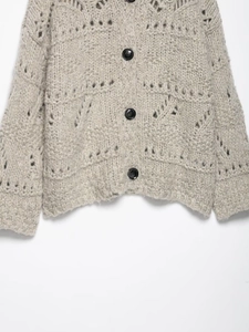 Detail of loose hollow knit cardigan with black buttons and textured pointelle pattern