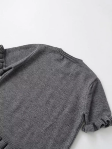 Dettaglio di un top grigio in maglia a maniche corte con bordi a balze decorativi