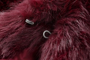 Macro detail of wine red faux fur vest featuring a silver metal eyelet closure