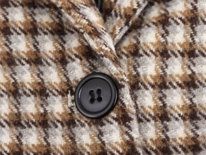 Macro view of plaid wool coat fabric with resin button and subtle gold thread detail