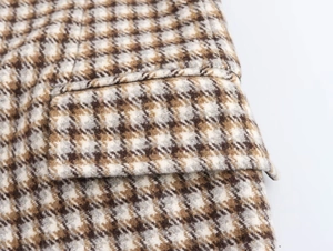 Detailed close-up of houndstooth plaid fabric and pocket flap on long wool coat