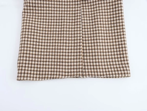 Close-up of the hem detail on a brown plaid long coat showing fine weaving and stitching