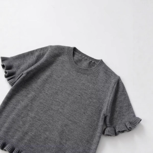 Top in maglia grigia a maniche corte con girocollo e orlo a balze su sfondo chiaro