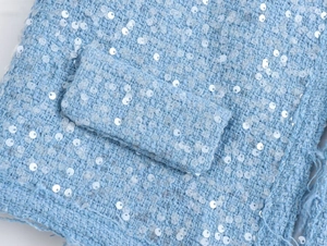 Close-up of light blue tweed fabric with shimmering sequins and pocket flap detail