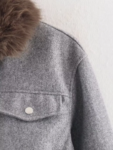 Détail de veste en laine grise avec col en fourrure marron et bouton métallique argenté
