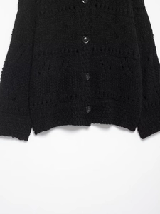 Close-up of black hollow-out knit cardigan showing textured hem and round buttons