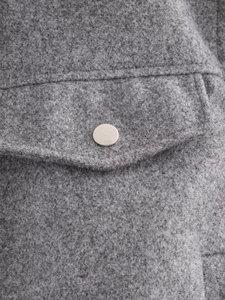Détail macro d'une veste en laine grise avec bouton-pression en métal argenté poli et poche