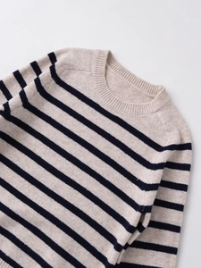 Detailed close-up of ribbed crewneck and navy stripes on beige knit sweater fabric