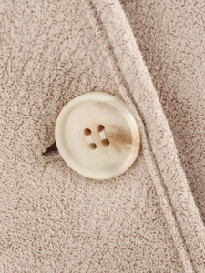 Macro detail of marble-textured button and oatmeal thick wool fabric on a women jacket