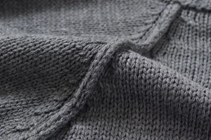 Detailed macro shot of grey chunky knit fabric texture showing high-quality wool yarn patterns