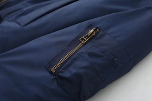 Macro detail of navy blue bomber jacket sleeve featuring a bronze metal zipper pocket