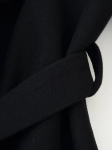 Detailed close-up of a black wool coat featuring a waist belt and textured fabric finish
