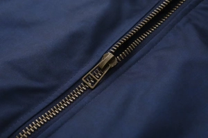 Detailed close-up of a bronze metal zipper on a dark blue vintage cotton jacket