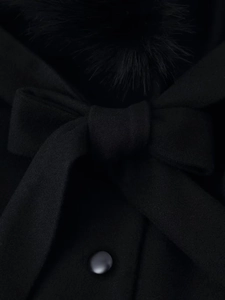 Detailed macro view of black wool coat featuring a large bow and soft faux fur collar