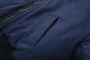 Detail of navy bomber jacket featuring a bronze metal zipper and smooth pocket flap