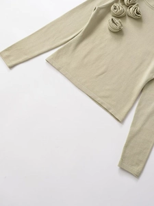 Detail of 3D rose flower decorations on a light green slim fit knitted long sleeve top